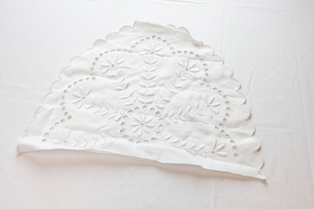 Hvit, halvsirkelformet brikke med brodert blomstermotiv.