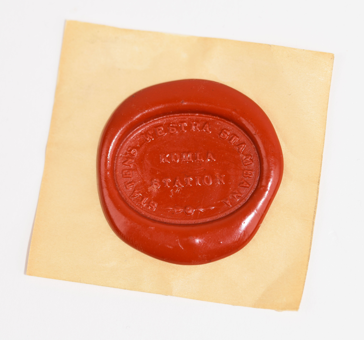 Metallstämpel med svarvat trähandtag. Oval fot av mässing med texten "STATENS WESTRA STAMBANA KUMLA STATION". Följande märkning finns på ovansidan "XII/136".