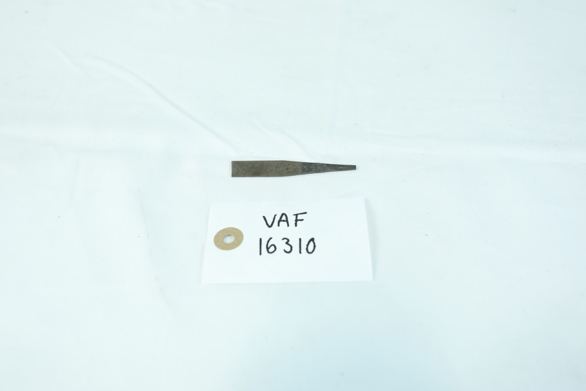 Liten metallgjenstand. Delvis rektangulært med innsmalning på den ene siden. Skrift på smalere del.
