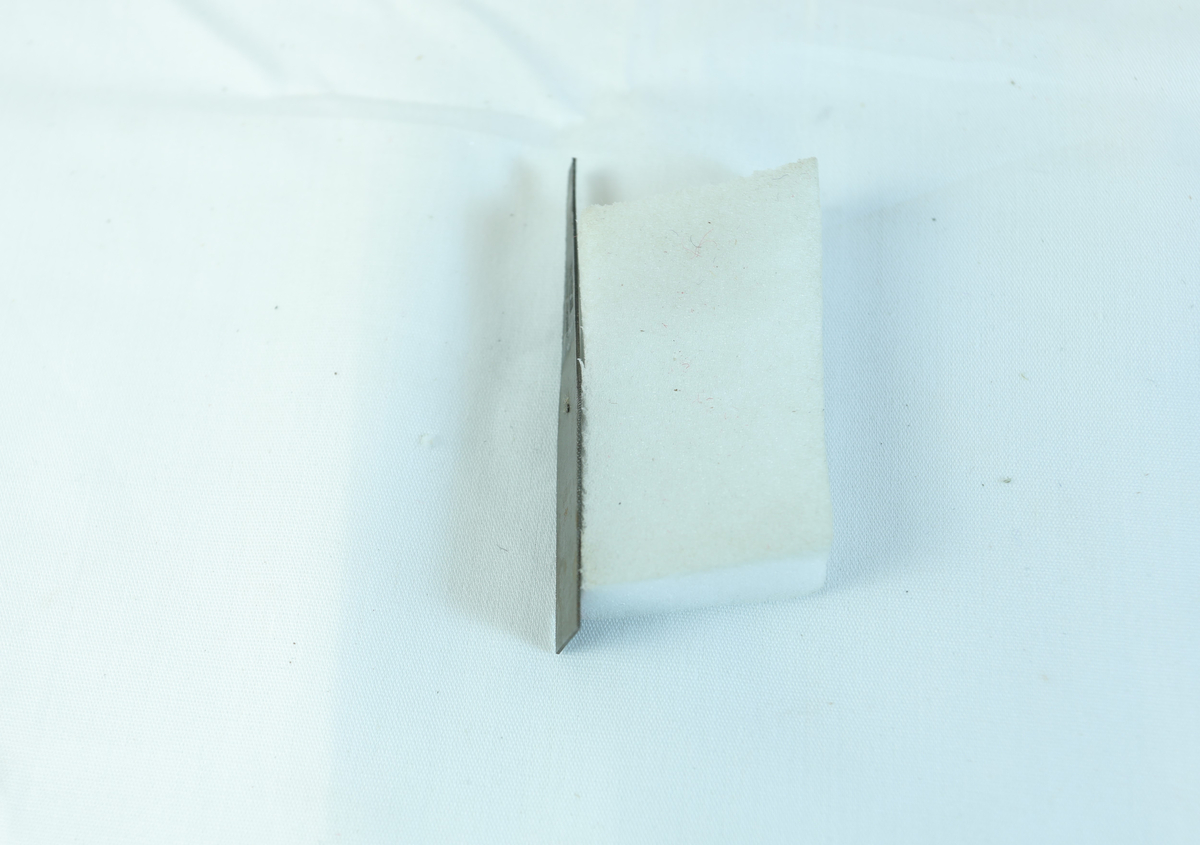 Liten metallgjenstand. Delvis rektangulært med innsmalning på den ene siden. Skrift på smalere del.