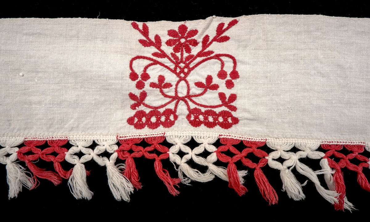 Hängkläde i vit lärft (bomull?), dekorerat med broderi i hallandssöm med rödfärgad bomullstråd. Broderierna består av två omväxlande mönsterpartier som upprepas sammanlagt nio gånger längs klädets längd – det ena mönstret fyra gånger, det andra två gånger. Strax till höger om mittpartiet finns ett monogram i korsstygn: "ABND" (troligtvis Anna Brita Nilsdotter). Hängklädet är tillverkat i ett stycke. Längs den nedre kanten löper en bård med knuten frans – varannan knut röd och varannan vit.