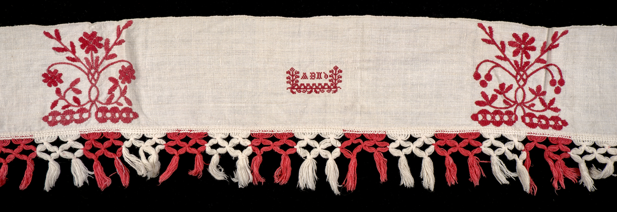 Hängkläde i vit lärft (bomull?), dekorerat med broderi i hallandssöm med rödfärgad bomullstråd. Broderierna består av två omväxlande mönsterpartier som upprepas sammanlagt nio gånger längs klädets längd – det ena mönstret fyra gånger, det andra två gånger. Strax till höger om mittpartiet finns ett monogram i korsstygn: "ABND" (troligtvis Anna Brita Nilsdotter). Hängklädet är tillverkat i ett stycke. Längs den nedre kanten löper en bård med knuten frans – varannan knut röd och varannan vit.