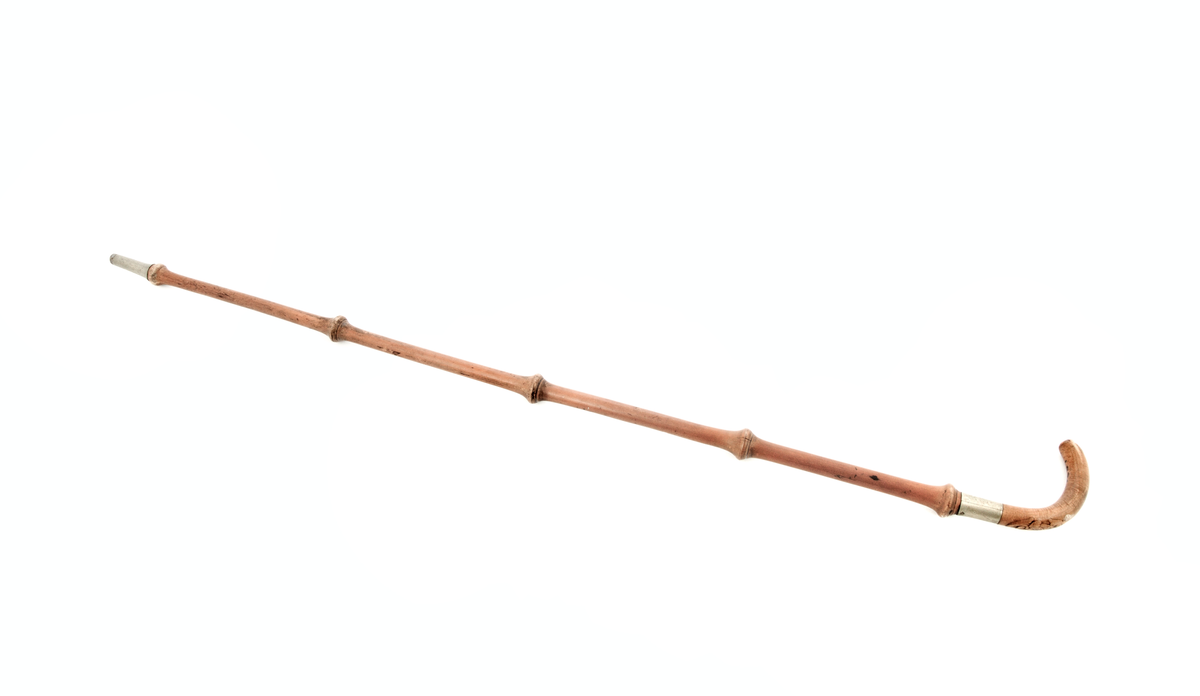 Bambusrør med 4 ledd. Nede i enden ein holk av nysylv og spiss av jern. Øvst er det ein slak krok av lønn, kroken gjeng ned i ein nysølv-holk som er nagla fast til  bambusrøret. Utskore rose på bøygen og i enden.