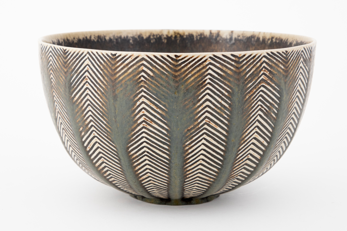 Bolle i glasert steingods. Sirkulær fot og vid åpning. Innsiden er grå med spetter og ujevn gulhvit rand. Utenpå har bollen horisontalt sikk-sakk rillemønster i gulhvitt på grått, med tykkere brungrå vertikale striper lagt utenpå i midten av hver mønsterrapport. Slik kan det grafiske mønsteret oppfattes figurativt som stiliserte trær.