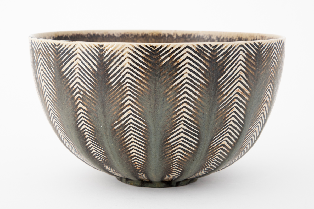 Bolle i glasert steingods. Sirkulær fot og vid åpning. Innsiden er grå med spetter og ujevn gulhvit rand. Utenpå har bollen horisontalt sikk-sakk rillemønster i gulhvitt på grått, med tykkere brungrå vertikale striper lagt utenpå i midten av hver mønsterrapport. Slik kan det grafiske mønsteret oppfattes figurativt som stiliserte trær.