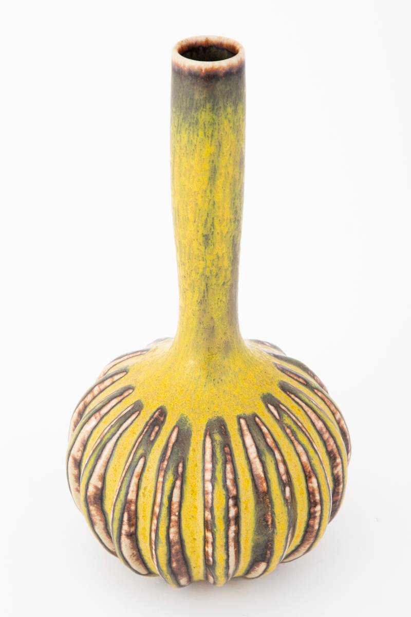Vase i steingods. Vasen har kuleformet korpus med lang, trang sylindrisk hals. Overflaten er dekket av gul glasur med grønnlig skjær. Korpus er dekorert med utstående, vertikale riller som er hvitlige med brune spetter. Munningsranden er brun.