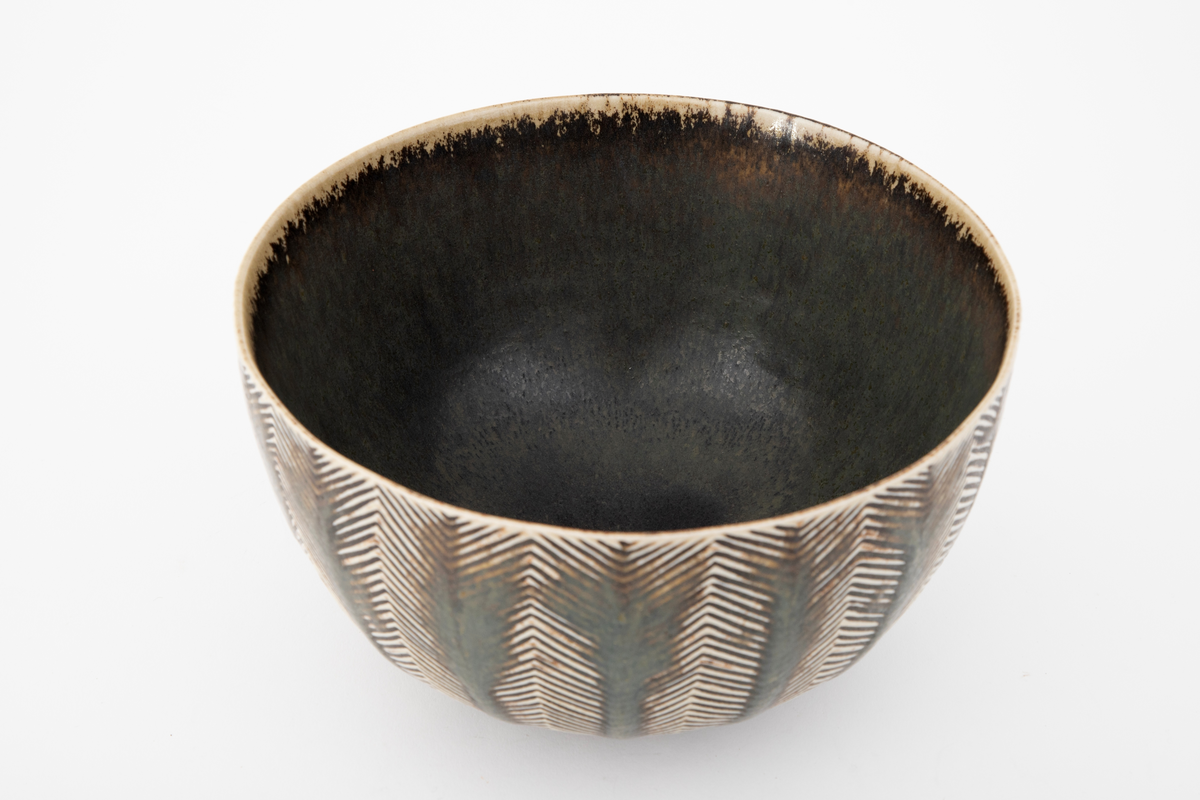 Bolle i glasert steingods. Sirkulær fot og vid åpning. Innsiden er grå med spetter og ujevn gulhvit rand. Utenpå har bollen horisontalt sikk-sakk rillemønster i gulhvitt på grått, med tykkere brungrå vertikale striper lagt utenpå i midten av hver mønsterrapport. Slik kan det grafiske mønsteret oppfattes figurativt som stiliserte trær.