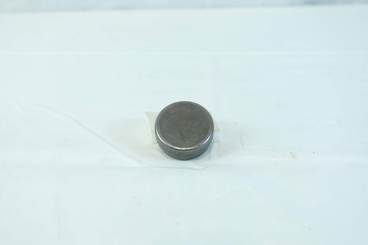 Etui i metall med rund form. I etuiet ligger det noen mindre metallstenger og flere små kors.