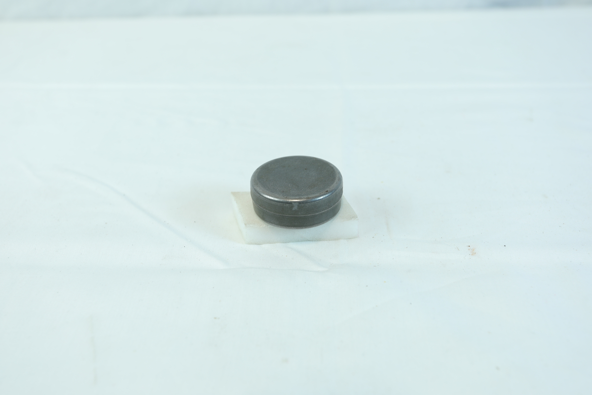 Etui i metall med rund form. I etuiet ligger det noen mindre metallstenger og flere små kors.