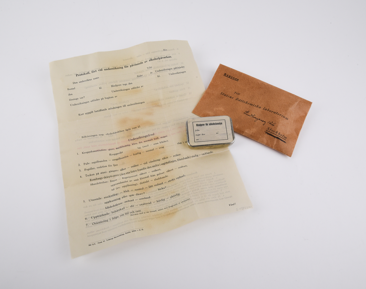 Kuvert med provtagningsset för blodprov för alkoholanalys med tillhörande protokoll.
Rektangulärt, brunt kuvert (:1) med text i svart som lyder "Express Till Statens Rättskemiska laboratorium Lindhagensg 126 Stockholm".
Protokoll (:2) som fylls i vid undersökningen. Rubriken lyder "Protokoll, fört vid undersökning för påvisande av alkoholpåverkan." Protokollet avslutas med en "Bruksanvisning vid tagandet av blodprov för alkoholbestämning.".
Ask i plåt (:3) med etikett på locket. Etikettens text i svart lyder "Blodprov för alkoholanalys från ... taget den ... kl. ... av ...". Asken innehåller bomull som skyddar tre glasrör och sex gummidetaljer.