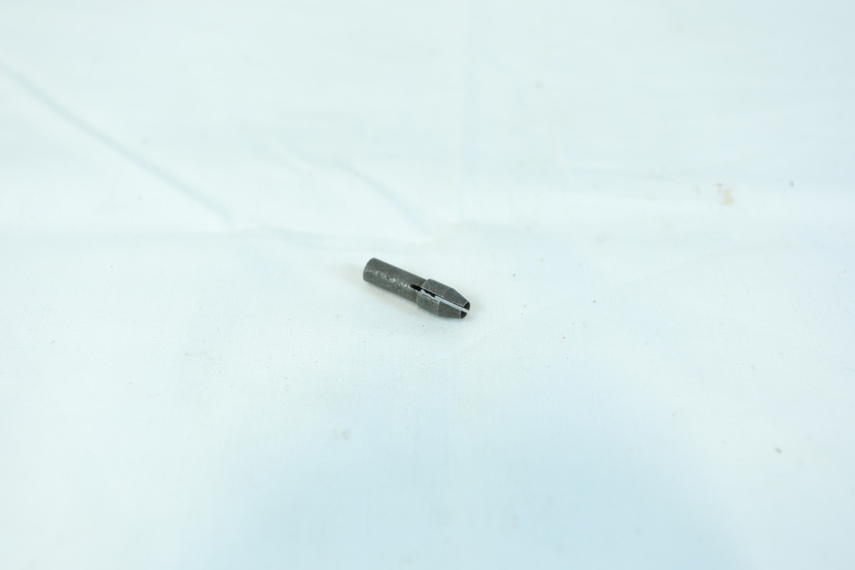En liten metallgjenstand, trolig en skrutrekkerbit, med sekskantet ende og flat spiss.