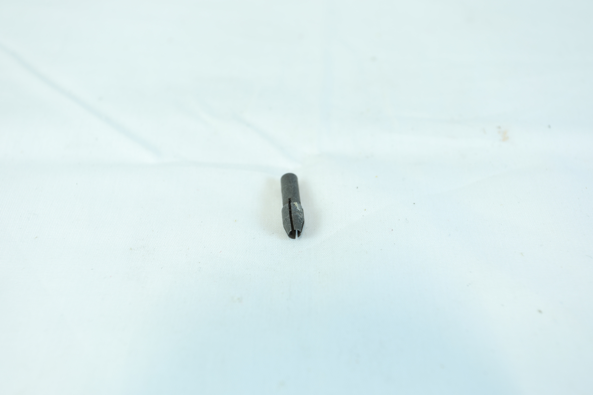 En liten metallgjenstand, trolig en skrutrekkerbit, med sekskantet ende og flat spiss.
