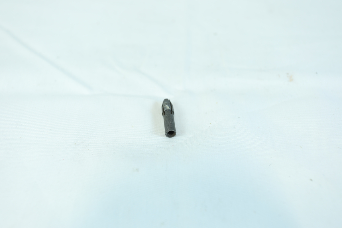 En liten metallgjenstand, trolig en skrutrekkerbit, med sekskantet ende og flat spiss.