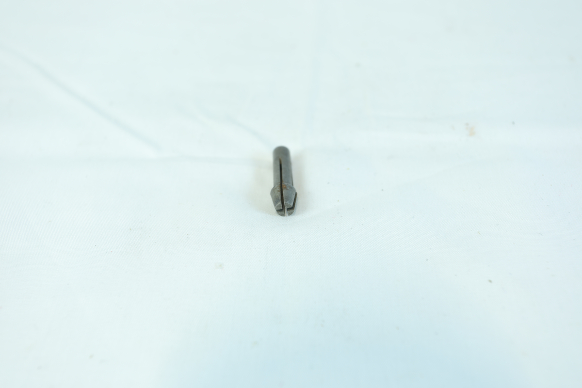 En liten metallgjenstand, trolig en skrutrekkerbit, med sekskantet ende og flat spiss.