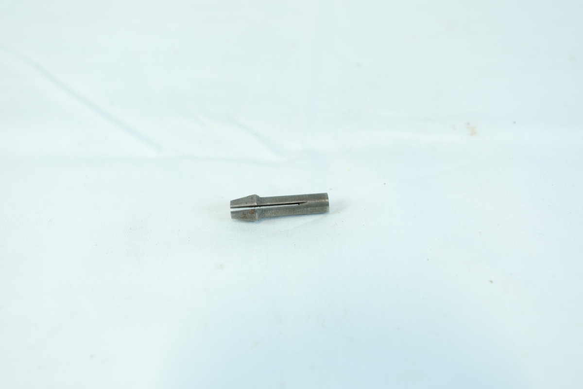 En liten metallgjenstand, trolig en skrutrekkerbit, med sekskantet ende og flat spiss.