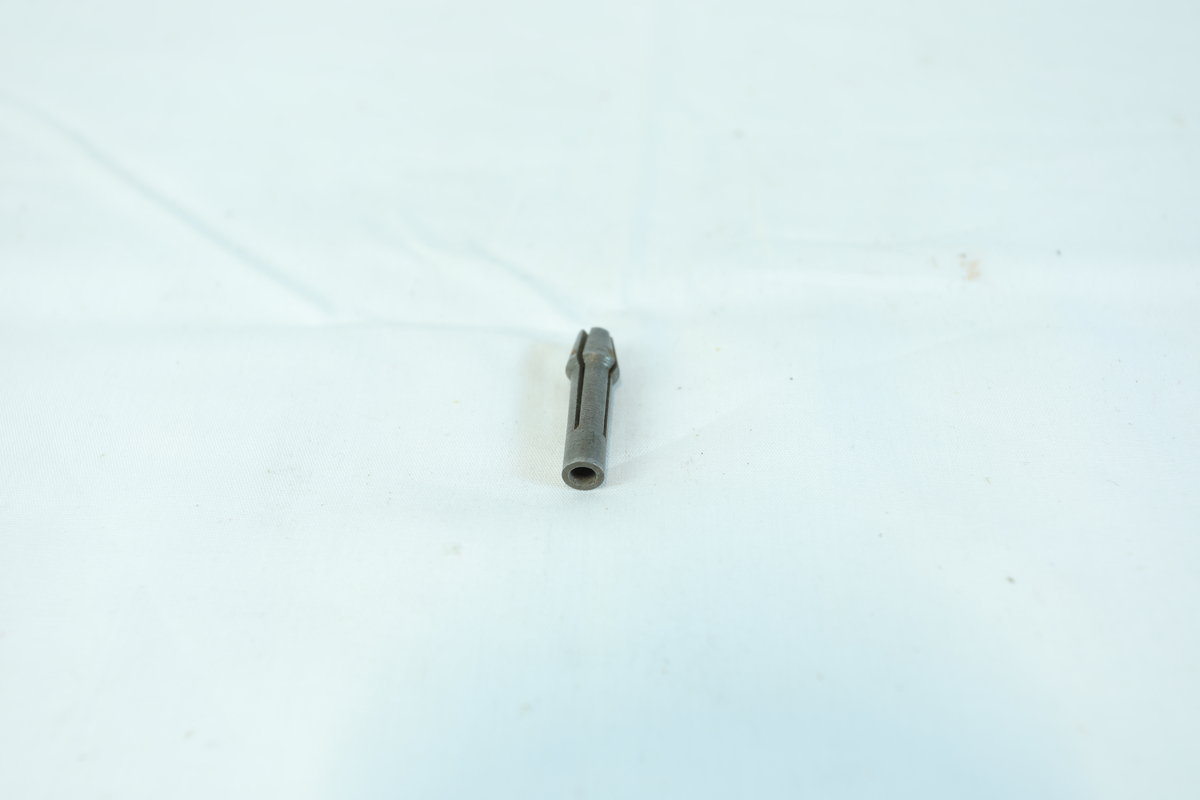 En liten metallgjenstand, trolig en skrutrekkerbit, med sekskantet ende og flat spiss.