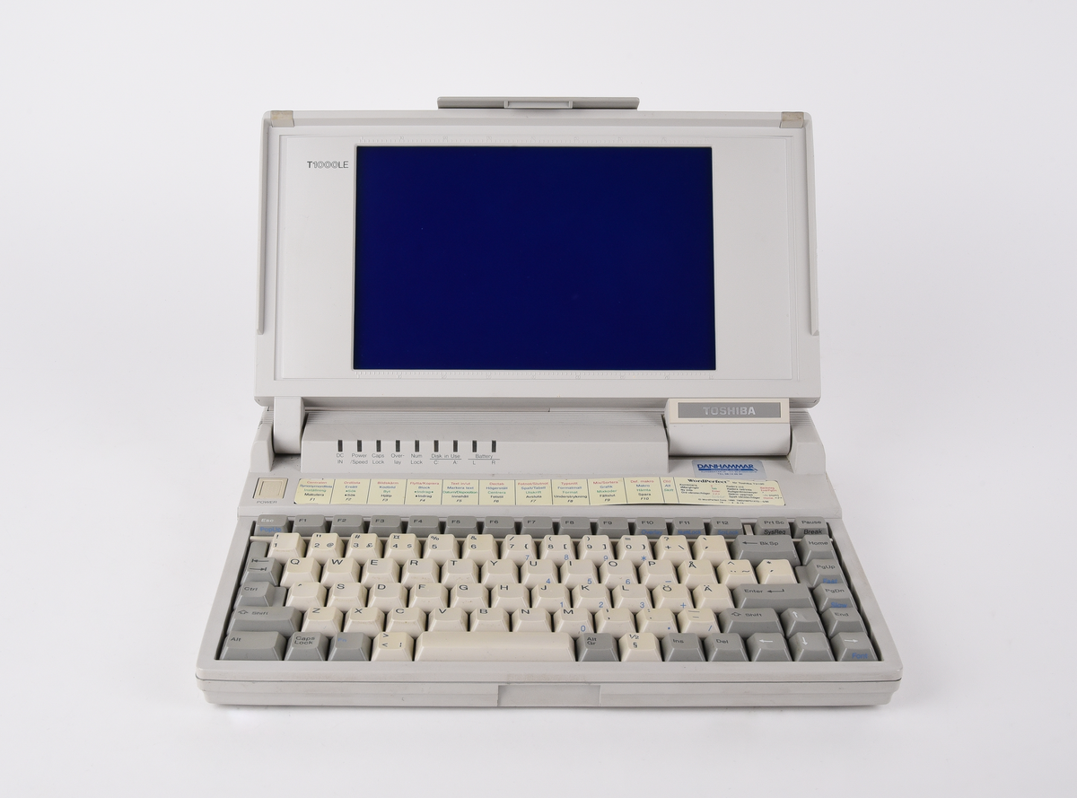 Bärbar dator (:1) Toshiba "T1000LE" av grå plast. Uppfällbar bildskärm som i uppfällt läge tillgängliggör tagentbordet med QWERTY-layout och svenska tecken. Löstagbar pappersremsa med kortkommandon ovanför tagentbordet. På sidan en port för 3,5-tums disketter. På baksidan en port till laddningsdocka (:2), även denna i grå plast. Laddningsdockan har ett flertal uttag till olika kablar, bland annat till en strömadapter (:3) i svart plast med tillhörande kabel. 
Två tillhörande 3,5-tums disketter (:4-5) även dessa från Toshiba. Med operativsystemet MS-DOS 3.3. Fyra tillhörande användarmanualer (:6-9). En manual med allmän information för den bärbara datorn på svenska. En manual för MS-DOS 3.3, en för den bärbara datorn och en för laddningsdockan, samtliga på engelska.