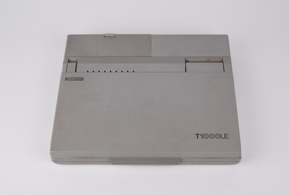 Bärbar dator (:1) Toshiba "T1000LE" av grå plast. Uppfällbar bildskärm som i uppfällt läge tillgängliggör tagentbordet med QWERTY-layout och svenska tecken. Löstagbar pappersremsa med kortkommandon ovanför tagentbordet. På sidan en port för 3,5-tums disketter. På baksidan en port till laddningsdocka (:2), även denna i grå plast. Laddningsdockan har ett flertal uttag till olika kablar, bland annat till en strömadapter (:3) i svart plast med tillhörande kabel. 
Två tillhörande 3,5-tums disketter (:4-5) även dessa från Toshiba. Med operativsystemet MS-DOS 3.3. Fyra tillhörande användarmanualer (:6-9). En manual med allmän information för den bärbara datorn på svenska. En manual för MS-DOS 3.3, en för den bärbara datorn och en för laddningsdockan, samtliga på engelska.