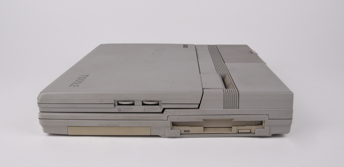 Bärbar dator (:1) Toshiba "T1000LE" av grå plast. Uppfällbar bildskärm som i uppfällt läge tillgängliggör tagentbordet med QWERTY-layout och svenska tecken. Löstagbar pappersremsa med kortkommandon ovanför tagentbordet. På sidan en port för 3,5-tums disketter. På baksidan en port till laddningsdocka (:2), även denna i grå plast. Laddningsdockan har ett flertal uttag till olika kablar, bland annat till en strömadapter (:3) i svart plast med tillhörande kabel. 
Två tillhörande 3,5-tums disketter (:4-5) även dessa från Toshiba. Med operativsystemet MS-DOS 3.3. Fyra tillhörande användarmanualer (:6-9). En manual med allmän information för den bärbara datorn på svenska. En manual för MS-DOS 3.3, en för den bärbara datorn och en för laddningsdockan, samtliga på engelska.