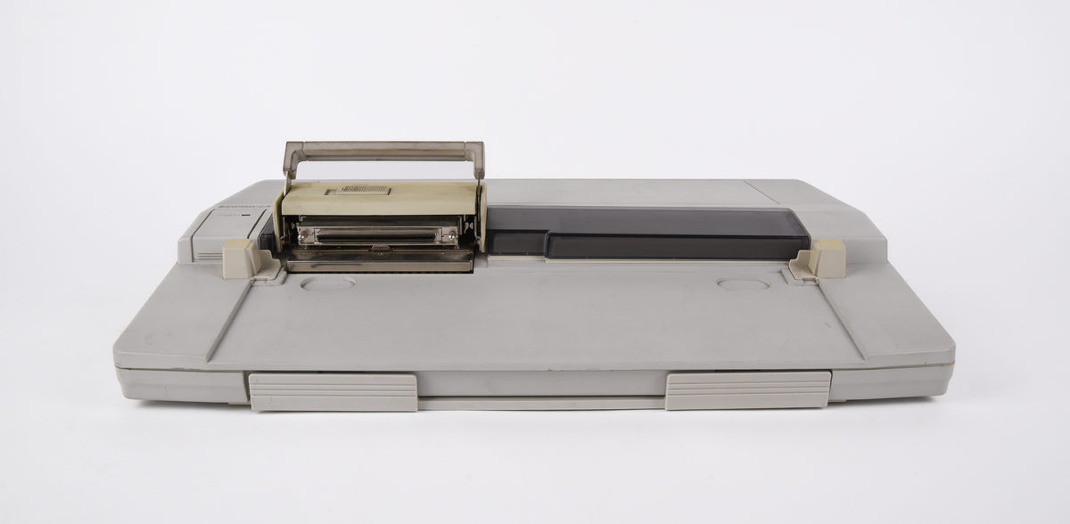 Bärbar dator (:1) Toshiba "T1000LE" av grå plast. Uppfällbar bildskärm som i uppfällt läge tillgängliggör tagentbordet med QWERTY-layout och svenska tecken. Löstagbar pappersremsa med kortkommandon ovanför tagentbordet. På sidan en port för 3,5-tums disketter. På baksidan en port till laddningsdocka (:2), även denna i grå plast. Laddningsdockan har ett flertal uttag till olika kablar, bland annat till en strömadapter (:3) i svart plast med tillhörande kabel. 
Två tillhörande 3,5-tums disketter (:4-5) även dessa från Toshiba. Med operativsystemet MS-DOS 3.3. Fyra tillhörande användarmanualer (:6-9). En manual med allmän information för den bärbara datorn på svenska. En manual för MS-DOS 3.3, en för den bärbara datorn och en för laddningsdockan, samtliga på engelska.