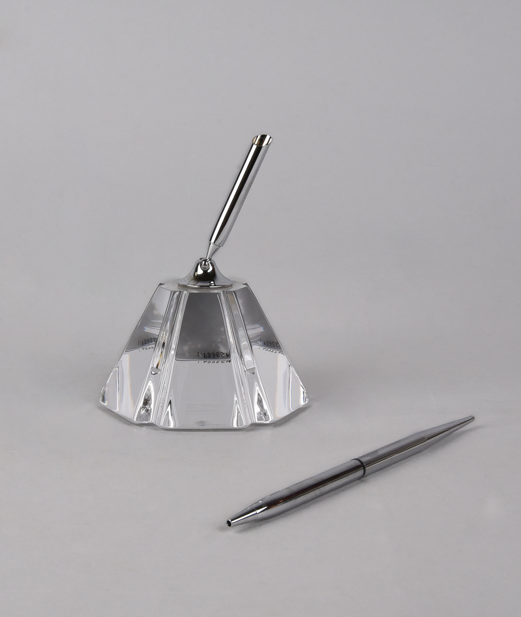 Pennställ (:1) av glas med penna (:2) i metall. Hållaren för pennan är också i metall och fäst på den lätt koniska glaskroppen. Graverad med Banverkets logotyp och text "BANVERKET" och "orrefors" undertill.