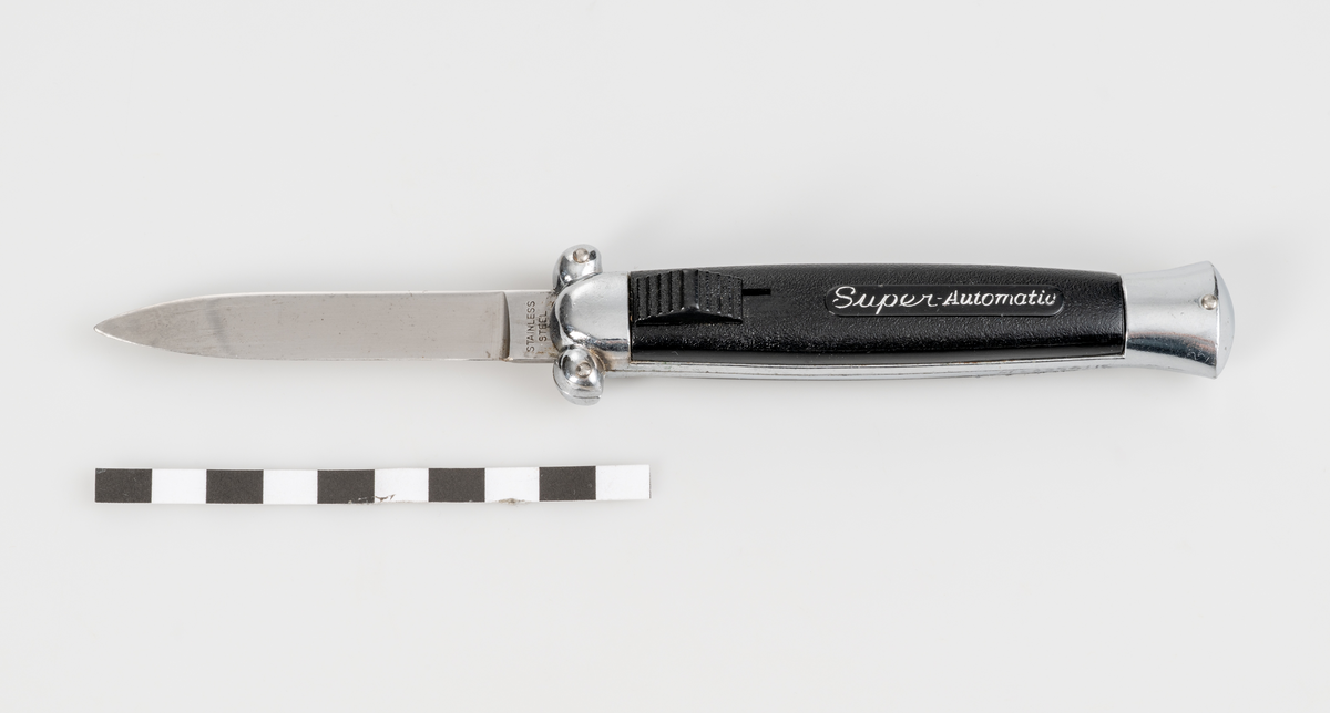 Stilettkniv. Knivblad i bajonettstil som frigörs framåt med skjutknappssystem. Svart knivskaft i plast.