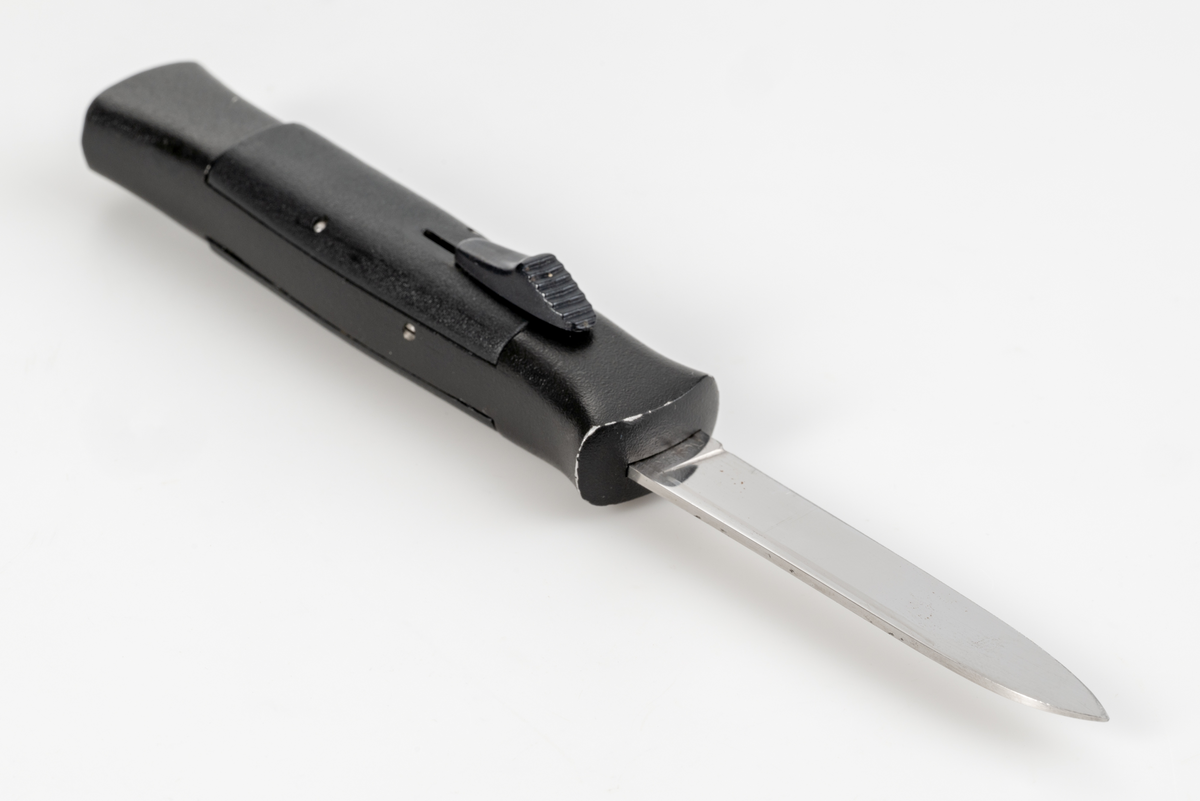Stilettkniv. Knivblad i bajonettstil som frigörs framåt med skjutknappssystem. Svart knivskaft.