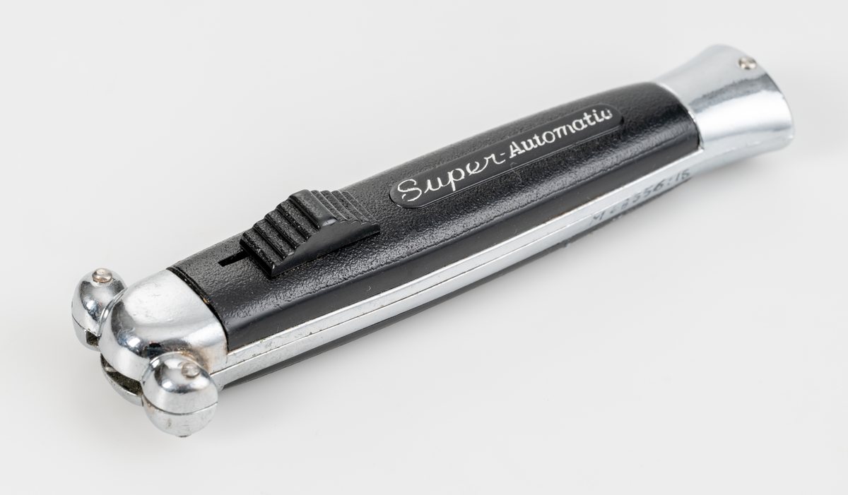 Stilettkniv. Knivblad i bajonettstil som frigörs framåt med skjutknappssystem. Svart knivskaft i plast.