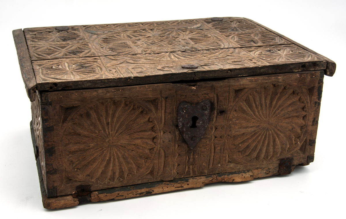 Skrin med fällock på smidda gångjärn. Hjärtformad nyckelskylt i järn. Låset borttaget. Botten fäst med metallbeslag. Skrinet är dekorerat med heltäckande karvsnittsdekor. På locket en stor och sex små karvsnittsrosetter. Även på sidorna karvsnittsrosetter. Alla olika. På locket vid låset bokstäverna "BSDS". Skrinet har troligen från början haft kulfötter i hörnen. Skrinet är bemålat inuti. I skrinet rött och i locket gult. Färgrester även på utsidan. 