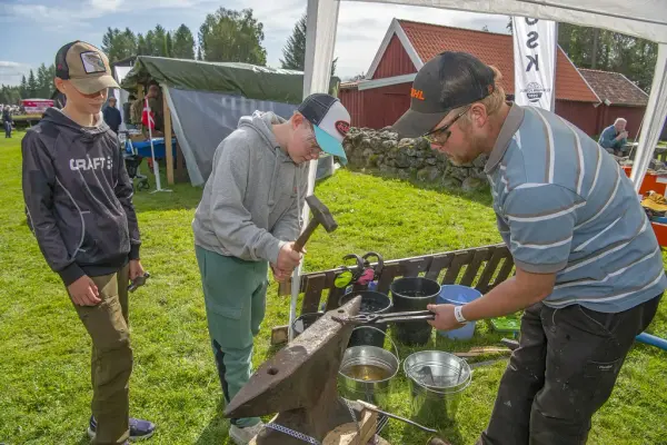 Mann holder en metallbit mens barn slår på med hammer og smir 
