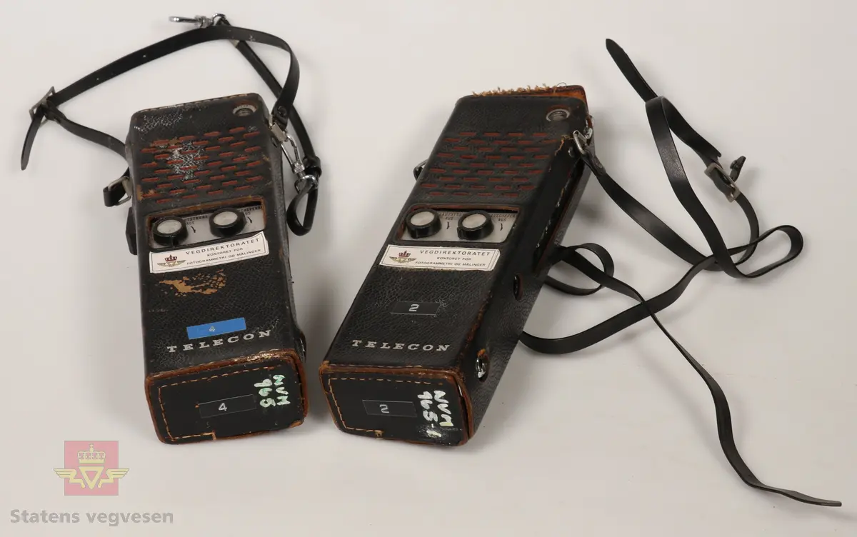 2 stk Walkie Talkie av plast og metall, sølv og svart farget. De er batteridrevet med uttak for 12V drift. Ligger i svarte lærhylstre. Merket med Vegdirektoratet. Lærreim for å bærbarhet. 
