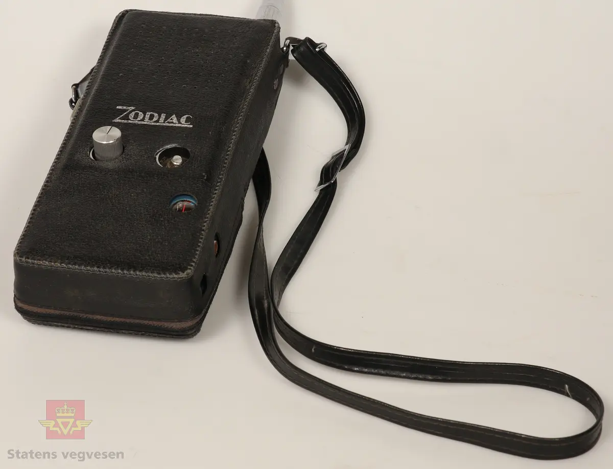 Svart, blå og blank Walkie Talkier. Drives av 8 stk AA batterier. Disse er fjernet. Den har tre kanaler. Skriften på gjenstanden er på tysk. Mangler en knapp. Defekt. Walkie Talkie ligger i svart skinnveske med glidelås og skinnreim. 