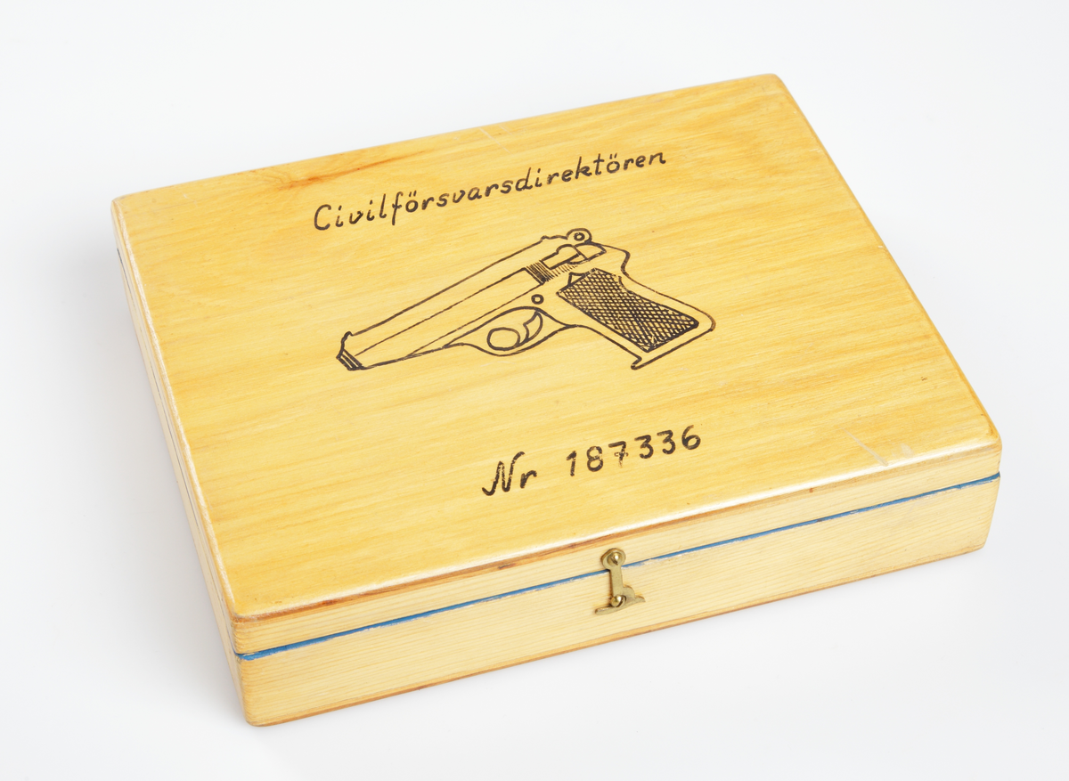 Pistollåda tillverkad i furu med sinkade hörn i både låda och lock. Botten och lockets översida i plywood. Locket har en avbildad pistol samt texten "Civilförsvarsdirektören" och "Nr 187336" i svart. Locket har två gångjärn i stål, och locket stängs med en mässingshasp och skruv. Insidan av lådan har ett avpassat fack för pistolen, och är inrett med tyg i plysch i blå färg. I lådan finns även en plåtask märkt "WALTHER" innehållande en flaska med vapenfett, samt en påse, även denna märkt med "WALTHER", med fetvadd och lin för vapenvård. Lådan innehåller också ett besikt-ningsprotokoll från 1979 som intygar vapnets kondition.
