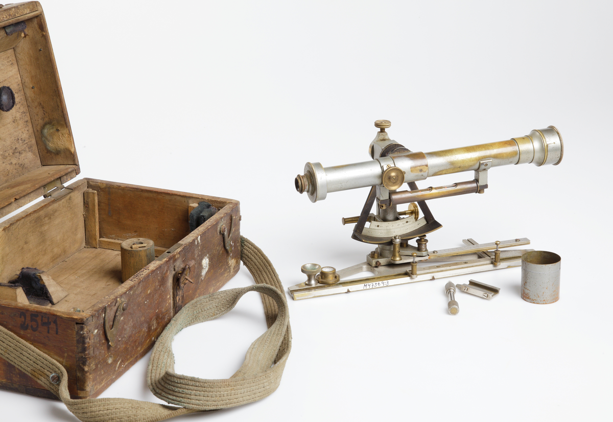 Mått: inst. tuben är 29,8 cm och ca 16,7 cm hög. Trpt. lådan är 33,5 x 13,5 x 20 cm.

Övriga uppgifter: optisk mätningsinstrument. Bestående av en linsförsedd mässingtub fäst på ett förnicklat mässingsstativ. Stativet har mätskalor samt två vattenpass. Ett är tubformat med två skalfönster, det andra, längre ner på stativets fot, är cirkeltunt och platt. 
Tillhörande transportlåda av trä med sinkade hörn, locket låses med två mässingshaspar. Sekundär bärrem av textil. 

Hela instumentet har vid användning varit placerat på ett stativförsett mätbord. 
Funktion: Avvägning och kartering av torrläggningsföretag