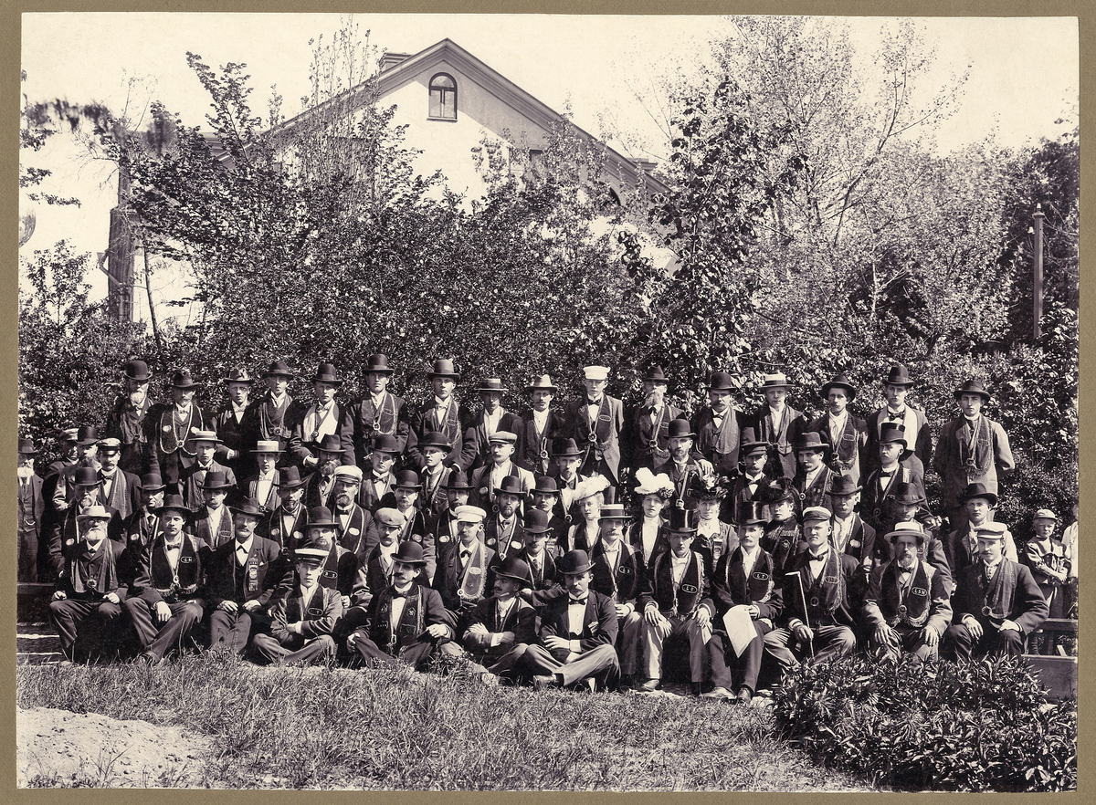 En stor grupp människor har samlats i en trädgård någonstan i Växjö, (Ulriksdal ?) för gruppfoto.
Text på baksidan: "Storlogemedlemmar af IOGT i Wexiö den 25.5. 1901".
