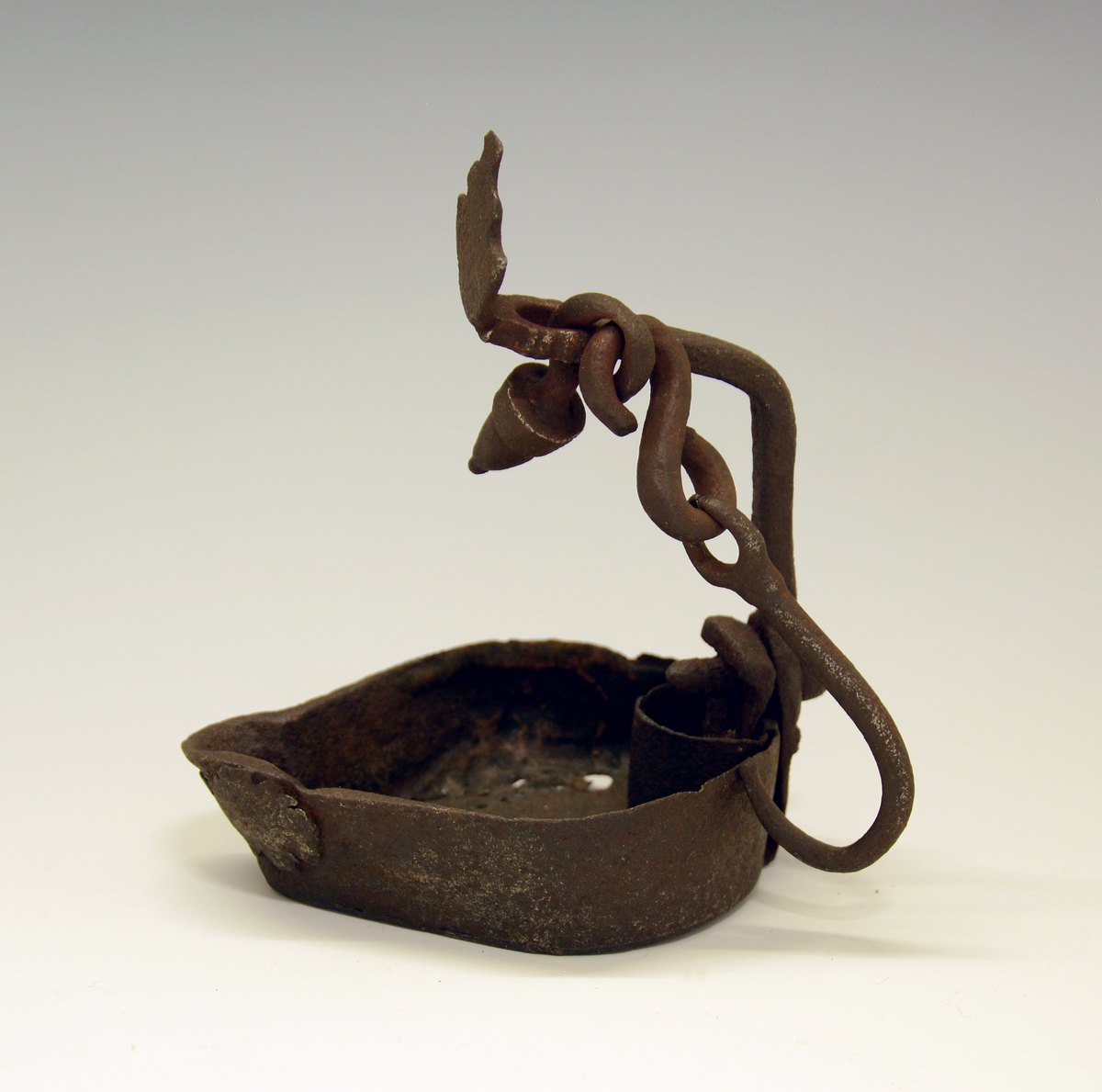 Tranlampe av jern, håndsmidd. Skålen med leppe foran og fold for hanken bak, hanken festet med nagle og mutter. Skjoldformet navneplate øverst.