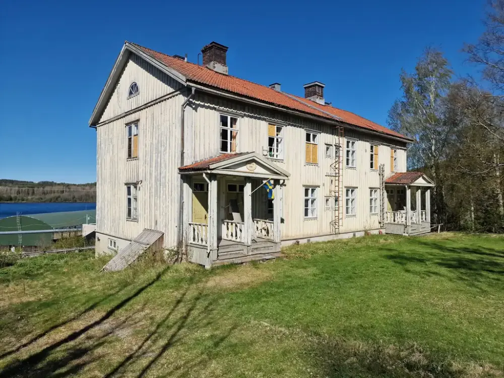 Ett vitt gammalt hus med tegeltak och blå himmel i bakgrunden.