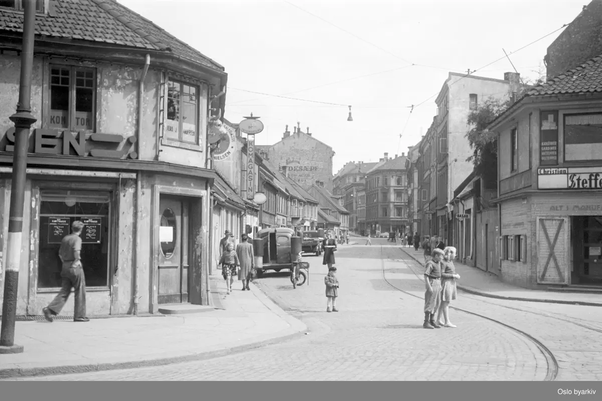 I Tøyengata 1 (t.h.) ser vi Grønland Manufaktur-Magasin, en klesbutikk som ble etablert av Christian Steffensen i 1892 og drevet frem til 1948. I Tøyengata 2 (t.v.) holdt kjøtt- og pølsemaker Jens J. Andersen til. .....