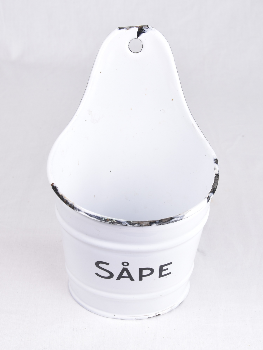 Hvit, emaljert metallbøtte med påskriften "SÅPE". Har hull til å monteres på vegg. Oval form.