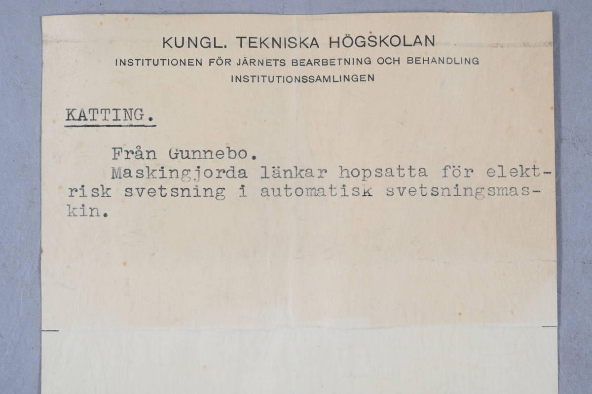 Prov på kätting. Tillhörande lapp med notering: "Kätting. Från Gunnebo. Maskingjorda länkar hopsatta för elektrisk svetsning i automatisk svetsningsmaskin."