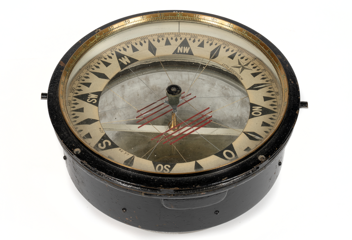 Luftkompass. Cylindrisk med graderad överkant. skål, cylindrisk del av svartmålad mässing, undre sfäriska delen av tjockt glas fylld med glycerin. Skiva med ringformad ros i grader (360) och streck samt nålsystem (8 st.) rödmålat. Rosen märkt: 'Lyth, Stockholm”. Skålen invändigt märkt: 'N:o 12087 
Glasets utsida märkt:  "Kelvin,Bottomley & Baird LTl. 16-20 Cambridges street Glasgow Patent N:o 22032 oz.” 
Har tillhört övningsskeppet "af Chapman”.