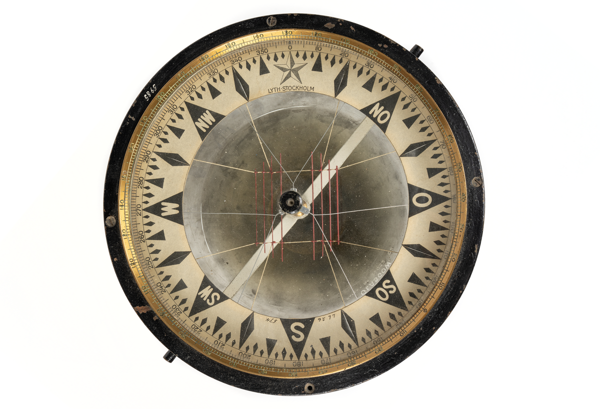Luftkompass. Cylindrisk med graderad överkant. skål, cylindrisk del av svartmålad mässing, undre sfäriska delen av tjockt glas fylld med glycerin. Skiva med ringformad ros i grader (360) och streck samt nålsystem (8 st.) rödmålat. Rosen märkt: 'Lyth, Stockholm”. Skålen invändigt märkt: 'N:o 12087 
Glasets utsida märkt:  "Kelvin,Bottomley & Baird LTl. 16-20 Cambridges street Glasgow Patent N:o 22032 oz.” 
Har tillhört övningsskeppet "af Chapman”.
