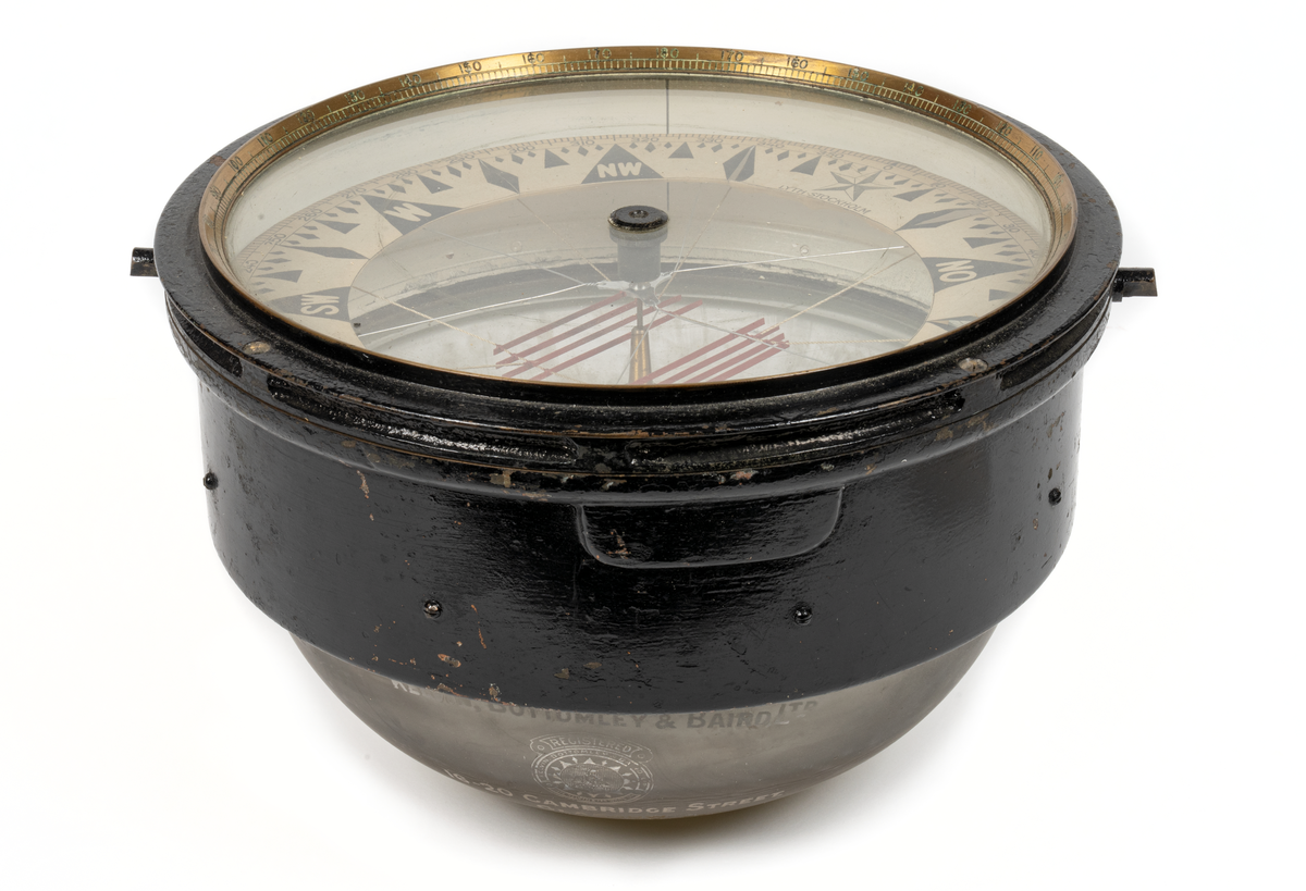 Luftkompass. Cylindrisk med graderad överkant. skål, cylindrisk del av svartmålad mässing, undre sfäriska delen av tjockt glas fylld med glycerin. Skiva med ringformad ros i grader (360) och streck samt nålsystem (8 st.) rödmålat. Rosen märkt: 'Lyth, Stockholm”. Skålen invändigt märkt: 'N:o 12087 
Glasets utsida märkt:  "Kelvin,Bottomley & Baird LTl. 16-20 Cambridges street Glasgow Patent N:o 22032 oz.” 
Har tillhört övningsskeppet "af Chapman”.