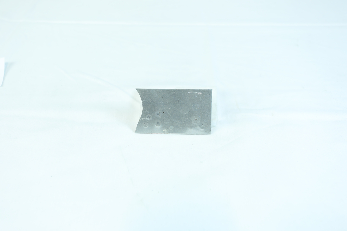 Firkantformet metallflate med sirkelformede merker. Trolig brukt som materiale i gullsmedvirksomhet. 