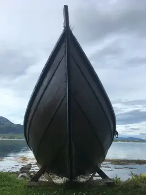 Bilde av en geitbåt på land tatt fra baugens side. I bakkant ser vi fjorden og fjell