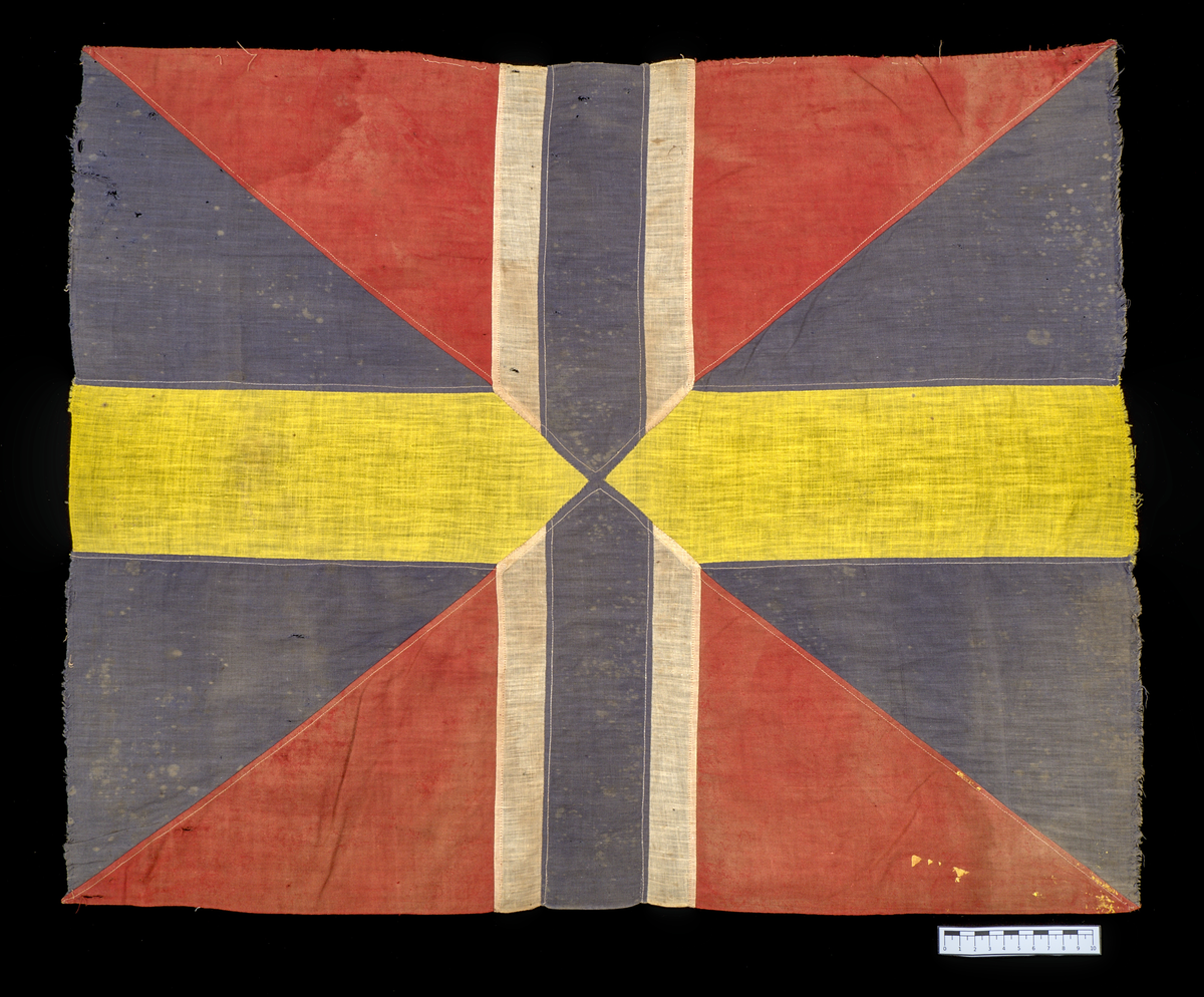 Unionsmärke från svensk-norsk flagga (1844–1905)

Rektangulärt tygmärke, sammansatt av flera tygstycken i tuskaftad bomull, som tillsammans bildar ett korslagt mönster av färgfält i rött, blått, vitt och gult. Styckena är sammanfogade med maskinsydda sömmar i vit bomullstråd.

Föremålet är skört, blekt och delvis nedfläckat med färg. Kaststygnen längs kanterna tillkom i samband med konservering år 2025.
