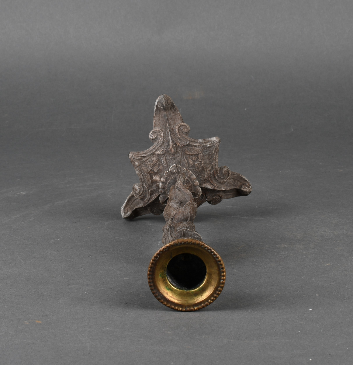 Lysestake av metall. Den har skaft formet som en kvinne som holder en lyre i venstre hånd. Hun står på et trefotet fotstykke. Øverst med pipe formet som en urne med perlebord langs kanten. Hele overflaten på lysestaken har støpt dekor.