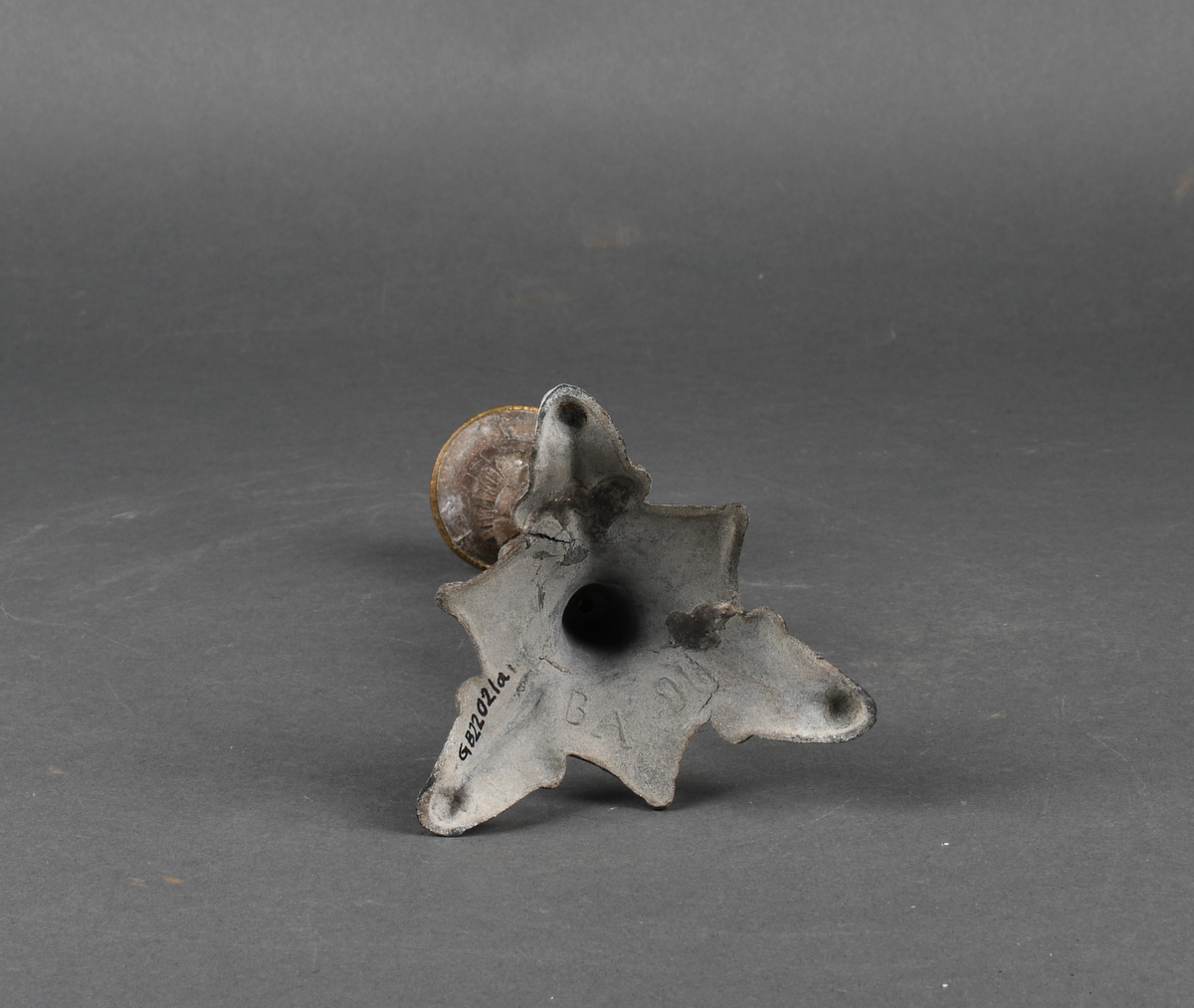 Lysestake av metall. Den har skaft formet som en kvinne som holder en lyre i venstre hånd. Hun står på et trefotet fotstykke. Øverst med pipe formet som en urne med perlebord langs kanten. Hele overflaten på lysestaken har støpt dekor.