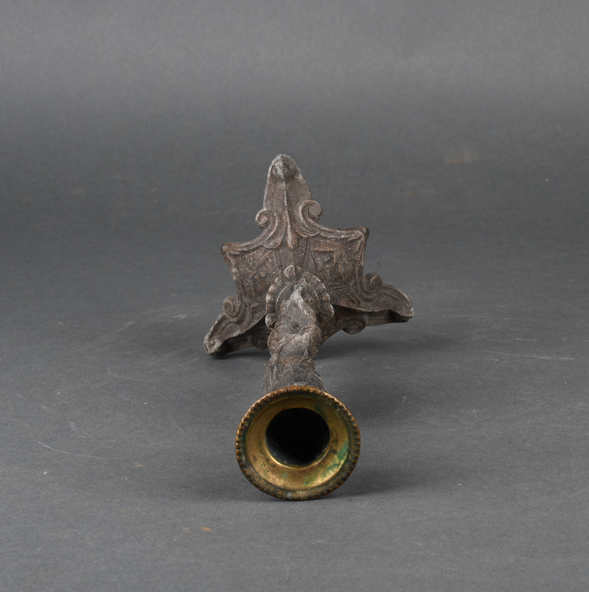Lysestake av metall. Den har skaft formet som en kvinne som holder en lyre i venstre hånd. Hun står på et trefotet fotstykke. Øverst med pipe formet som en urne med perlebord langs kanten. Hele overflaten på lysestaken har støpt dekor.