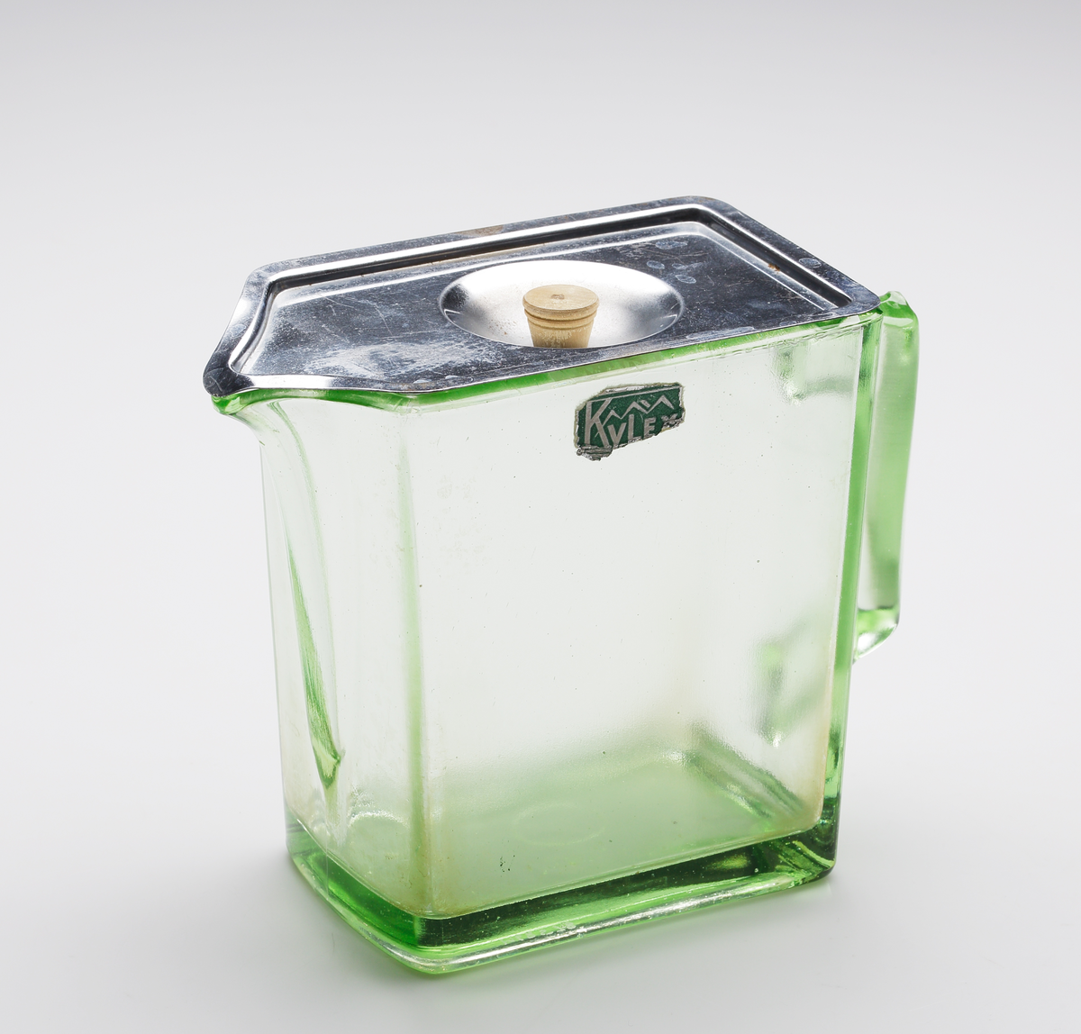 Ljusgrön kanna med metallock för kylskåp. Formgiven av William Stenberg 1938. Raktangulär med grep och snip på kortsidorna.
